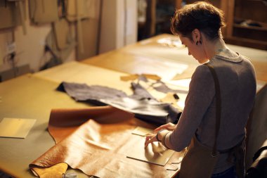 Esnaf, atölyede alet ve malzemelerle süslenmiş deri eşyalar yapıyor. Deri kumaşlı titiz bir işe odaklanan kişi detaylara önem verir.