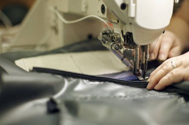 El işleten dikiş makinesi iğne altında kumaşa özenle rehberlik ediyor ve iyi aydınlatılmış çalışma alanında hassasiyet ve kalite dikişi sağlıyor.