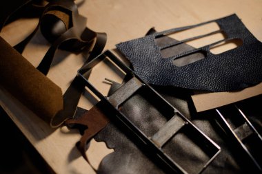 Eller, aksesuar yapmak için deri parçaları kesmek için alet kullanıyor. Deri parçalarının çeşitli tonları ve dokuları metal aletlerin yanında karmaşık tasarımlar yaratıyor.