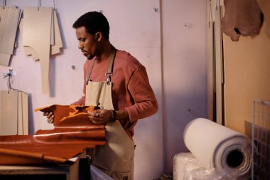 Becerikli bir zanaatkar atölyede çeşitli deri aletlerle süslenmiş deri parçaları üzerinde dikkatle çalışıyor. Doğal doku ve titiz süreç yüksek kaliteli özel ögeler oluşturur