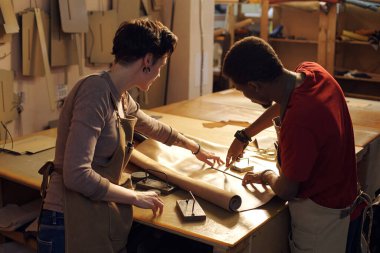 Atölye ortamında kağıt kalıpları üzerinde çalışan iki kişi. Her ikisi de odaklanmış durumda iken bir kişi bir talimat gösteriyor.