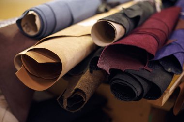 Resim, atölye ortamında farklı dokulara ve deri malzemelerin renklerine odaklanmış çeşitli deri parçalarını gösteriyor