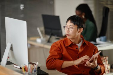 Çağdaş bir açık-plan ofisinde bilgisayarlı tablet üzerinde gayretli çalışan Asyalı çalışanlar arka planda görevlere odaklanırken,