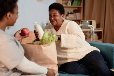 Orta dereceli mutlu siyahi kadın çantalarını açıyor ve kadın sosyal hizmet görevlisinden yardım alıyor. Evde yalnız yaşlılara yemek dağıtıyor.