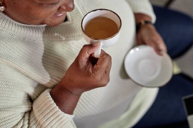 Arka plandaki büyükannenin seramik çay fincanından yeşil bitki çayı içerken, evde sıcak içeceklerin tadını çıkarırken, uzay fotokopisi çekerken yüksek açı çekimi.