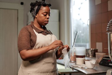 Orta boy Afrika kökenli Amerikalı fırıncı önlük giyer. Plastik eldivenler giyer. Küçük fırın mutfağında yemek yapmaya hazırlanır.