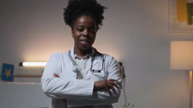 Dost canlısı genç zenci doktor portresi. Omuzlarında steteskop olan laboratuvar önlüğü giymiş. Akşamları çocuk hastanesi koğuşunda kameraya gülümsüyor.