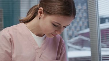 Pembe üniformalı, genç, konsantre olmuş beyaz kadın veterinerin, veteriner ofisindeki kalemin ışığını kullanarak, masadaki sevimli beyaz evcil tavşanın kulaklarını incelerkenki görüntüsünü aşağı eğ.
