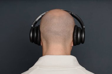 Kafası tıraşlı bir adamın kablosuz kulaklıkla podcast dinlediği arka plan stüdyoda gri arka plan karşısında duruyor, boşluğu kopyala