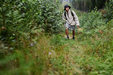 Geniş açı, genç Asyalı adamın erkek turist olarak ormanda yürüyüş yaptığını, patikayı takip ettiğini ve fotokopi alanının etrafına baktığını gösteriyor.