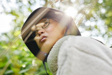 Genç Asyalı adamın güneş ışığı ışınlarıyla ormanı keşfederken gözlük takıp gözlerini kaçırdığı dramatik alçak açı görüntüsü.