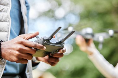 Erkek ellerinin dron kontrolörünü tutup düğmelere basarken açık havada teknolojik destekli videografinin tadını çıkarıyorum.