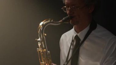 Orta yaşlı, siyah dumanlı sahnede müzik çalarken doğaçlama yapan beyaz erkek saksafoncudan esinlenmiştir.