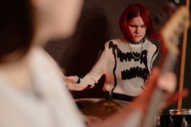 Medium shot of concentrated teenage female musician playing beat on drums while performing punk rock music with girls band in recording studio, copy space clipart