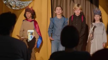 Dört çocuk aktörden oluşan bir grubun omuz üstü çekimleri sahnede duruyor, seyircilerin önünde eğiliyor.