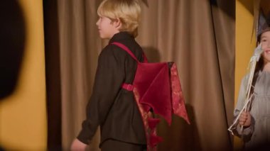 Okul tiyatrosunda kostüm giyen üç çocuğun el kamerasıyla çekilmiş bir fotoğrafı.