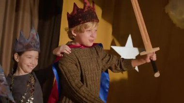 Bir grup neşeli erkek ve kız kostüm giymiş sahnede peri masalı karakterlerini oynarken eğleniyorlar.