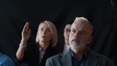 Çeşitli iş adamlarından oluşan bir grup toplantı sırasında sunumu dikkatle izliyor ve sorular soruyorlar.