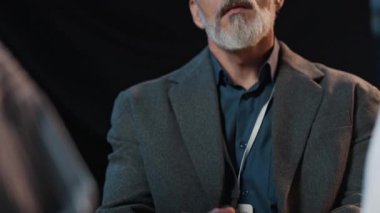 Orta yaşlı, beyaz takım elbiseli bir adam iş konferansında soru sormak için elini kaldırıyor.