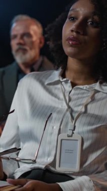 Dikey çekimde genç siyahi kadın iş konferansına katılıyor. Gözlüklerini çıkarıyor ve not alıyor.