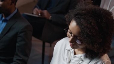 Genç Afrikalı Amerikalı iş kadınının yüksek açılı görüşü sandalyede oturup konuşmacıları dinlemesidir.