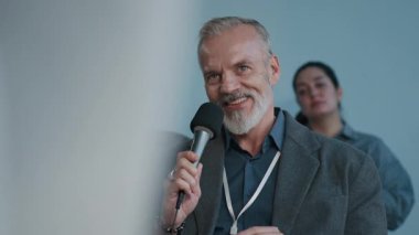 İş konferansı sırasında genç siyahi bayan meslektaşına mikrofon veren olgun beyaz bir adam.
