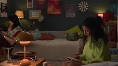 Etnik çeşitliliğe sahip iki kız geceyi yurt odalarında geçirip üniversite için ödev yapıyorlar.