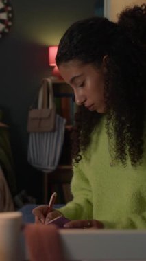 Yurt odasında oturan, yeşil süveter giyen melez genç bir kız not defterine yazıyor.