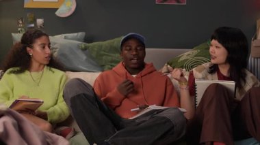 Üç farklı gen Z arkadaş grubu kanepede oturup okul projesi üzerinde çalışırken sohbet ediyorlar.