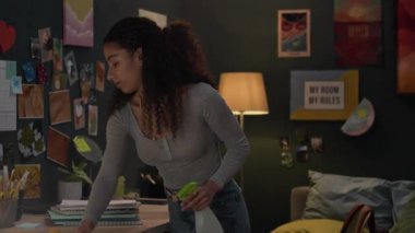 Çift ırklı genç bir kız, dağınık yurt odasında bir şişe deterjan temizleme masası tutuyor.