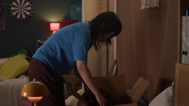 Yurt odasına taşınırken karton kutudan bir şeyler çıkaran genç Asyalı kız.