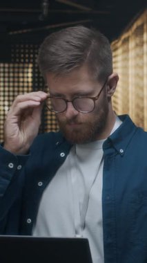 Kafkas asıllı genç erkek bilişim uzmanının dikey portresi. Gündelik kıyafet uzmanı. Gözlüklerini çıkarıyor ve kameraya gülümsüyor.