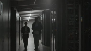 Modern veri merkezinde koridorda yürüyen genç beyaz bilişim uzmanlarının görüntülerini takip ediyorum. Sonra da sunucu odasına dizüstü bilgisayarların bakımını kontrol etmek için giriyorum.
