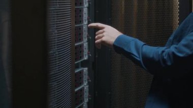 Modern veri merkezinde sunucu odasındaki ana bilgisayarın çalışmalarını kontrol eden günlük giysi ve gözlüklü genç beyaz bilişim mühendisinin yan görüntüsünü kaldır