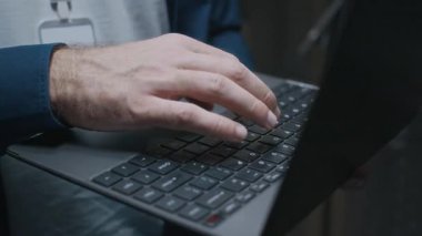 Gözlüklü, bilgisayar başında bilgisayar başında sunucu odasında duran ve veri merkezindeki donanımı kontrol eden genç, konsantre olmuş beyaz erkek bilişim teknisyeninin yakın çekim görüntüsü.