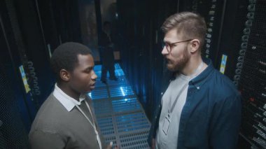 Sunucu odasında çalışan ve veri merkezinde çalışan el feneriyle donanımı kontrol etmeye başlayan çeşitli erkek bilişim teknisyenlerinin yüksek açılı görüntüsü.