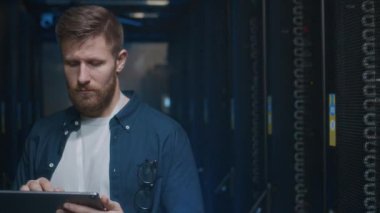 Tablet üzerinde kodlama yapan beyaz erkek bilişim mühendisinin odak noktası veri merkezindeki sunucu odasında genç Afrikalı Amerikalı erkek meslektaşıyla birlikte çalışıyor.