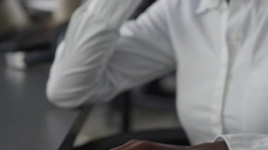 Kendine güvenen genç siyahi kadın yöneticinin masa başında otururken telefonla konuşurken ve açık uzay ofisinde bilgisayar üzerinde çalışırken yakın plan çekimleri.