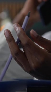 Beyaz tişörtlü genç Afro-Amerikan kadının ofiste çalışırken iş sözleşmesini tartışırken parmak uçlarında dönen kalemle dikey yavaş çekimi.
