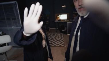 Olay yeri hakkında yorum yapmayı reddeden, olgun, beyaz erkek meslektaşlarıyla dava üzerinde çalışan haber muhabirlerinin mikrofonlarını kaplayan eldivenli genç siyahi kadın polis memurunun yavaş çekimleri.