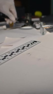 Steril eldivenli tanımlanamayan dedektifin dikey görüntüsü ofis masasında cımbız kullanarak kanıt topluyor, suç mahallinde çalışıyor.