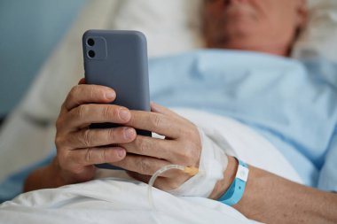 Hastanın hastane yatağında yatarken, elinde akıllı telefon, bileğinde tıbbi bileklik, sağlık hizmetlerinde yaşlıların kullandığı teknolojiyi gösteren görüntüler.
