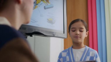 Asyalı kızın robot yapısının dijital tabletle tanınmayan öğretmenin önünde durup BTMM dersinde dikkatle dinlediği görüntüler.