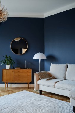 Oturma odasında modern mobilyalar sergileniyor. Şık dekorları var. Yuvarlak ayna, ahşap mobilyalar ve yer lambası da dahil. Boşluk rahat ve rahatlamak için uygun düzenlenmiş görünüyor.