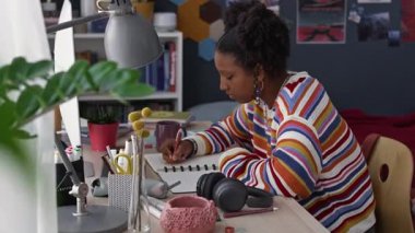 Bilgisayarın önündeki duvarda bir sürü posterle rahat odasında oturan ve interneti kullanarak ödev yapan konsantre siyahi kızın orta boy görüntüsü.