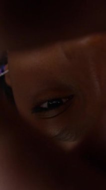 Düşünceli, renkli kazaklı genç bir kızın dikey yüksek açılı görüntüsü. Kameraya çapraz ellerle bakıyor. Kapalı alanda yerde yatıyor.