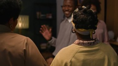 Siyahi etnik kökenli genç eşlerin, davetliler evlerine akşam yemeği için geldiklerinde nazik kucaklaşmalar ve öpücüklerle ailelerini selamladıkları orta boy bir fotoğraf.