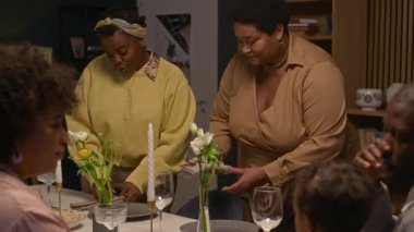 Yaşlı siyahi bir kadının evde aile kutlamaları sırasında neşeli bir şekilde sohbet ederken yetişkin bir kızla birlikte yemek masasında servis ettiği fotoğraftaki Dolly.