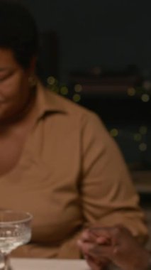 Siyahi, son sınıf öğrencisi bir kadının yemek öncesi dua ederken yetişkin çocuklarla yemek yerken birlikte yemek masasının etrafında otururken çekilen dikey fotoğrafı.