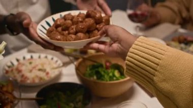 Yetişkin siyahi bir adam yemek masasında ailesiyle sohbet ediyor. Şenlikli ev yemeği sırasında bir tabak köfte yiyor.